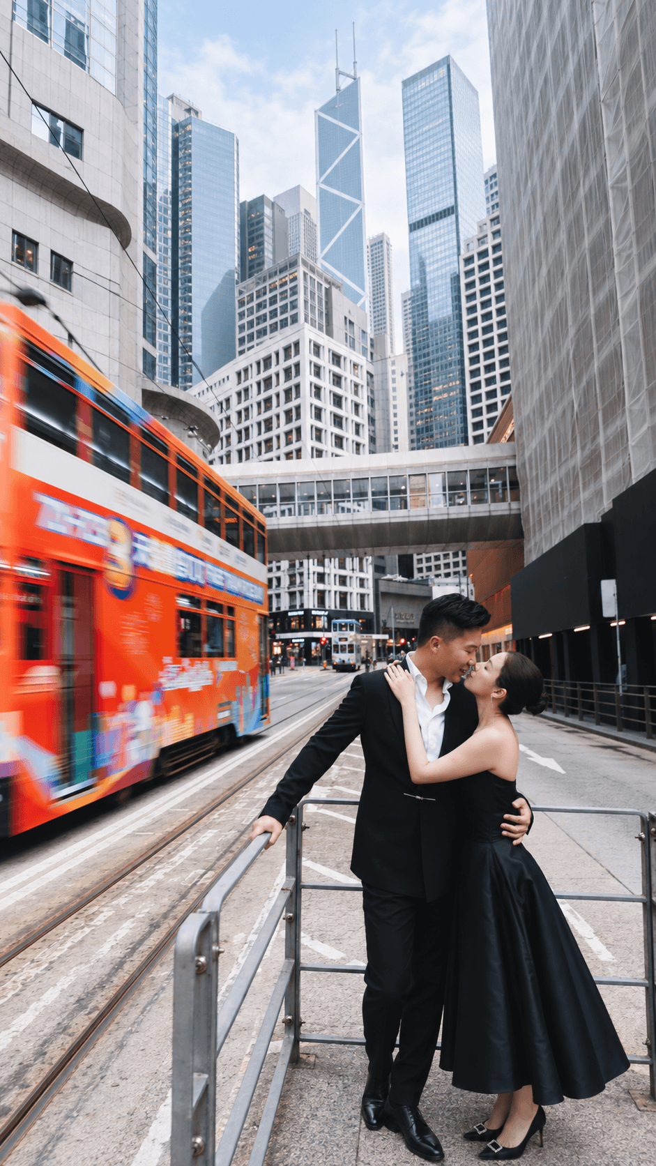 Natalie and Bryan embracing beside a moving red tram in Hong Kong