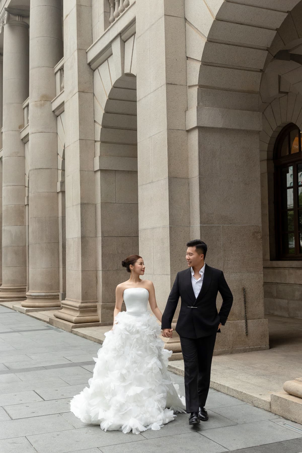 Natalie and Bryan walking hand in hand beneath grand stone arches