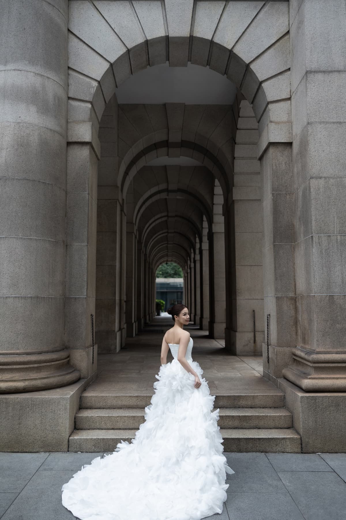 Natalie posing in her wedding gown beneath a grand stone arcade