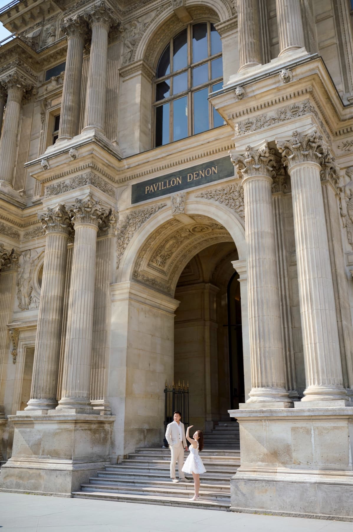 Natalie and Bryan standing beneath the ornate facade of the Pavillon Denon