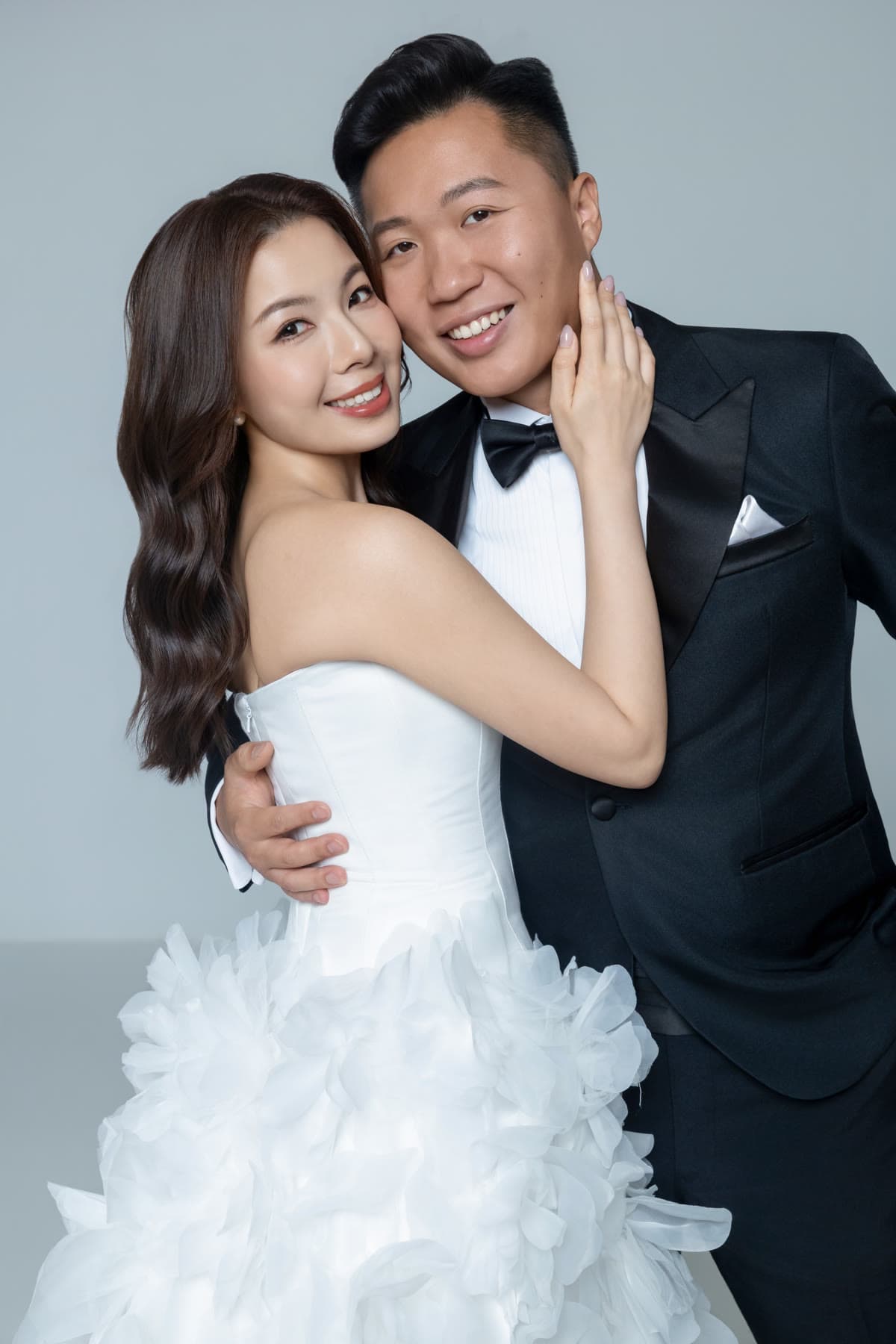 Natalie and Bryan embracing against a pale studio backdrop